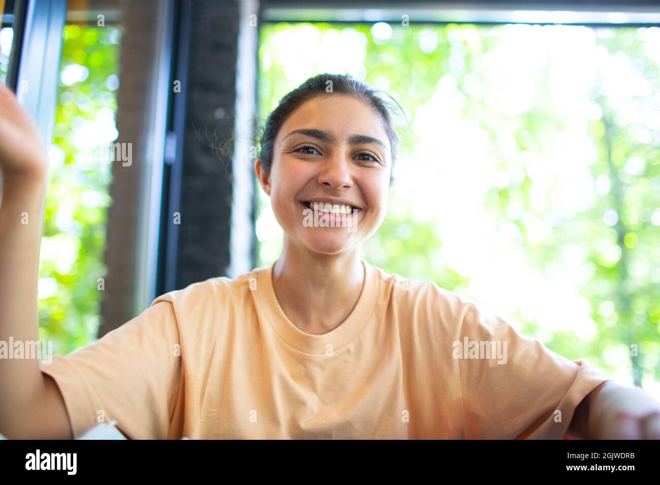 Headshot of indian woman sit on potdoor cafe waving hand looks to camera make video call chat use computer laptop webcam view, vlogger record webinar, job interview distantly concept. Stock Photo
