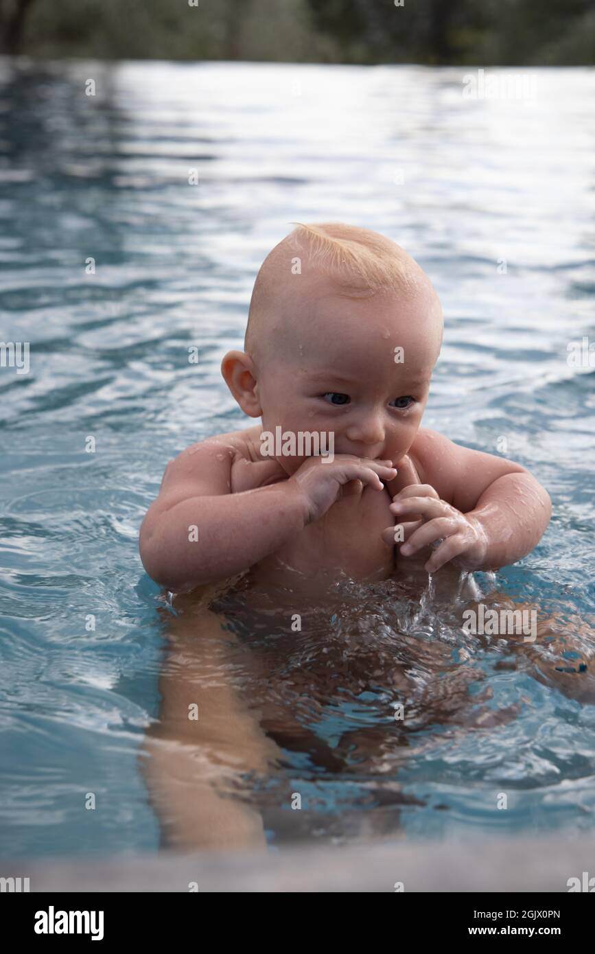 Beautiful, sweet baby boy swimming in the swimming pool holding fathers