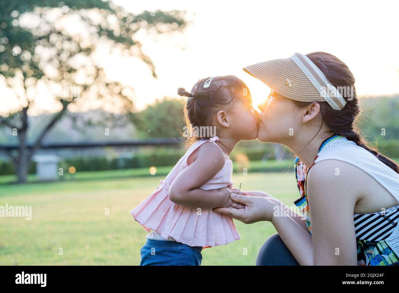 a thai mother kissing child with holding hands in green field under