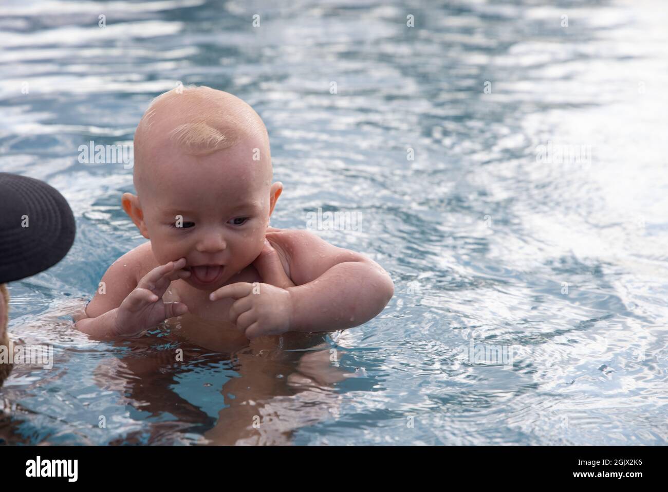 Beautiful, sweet baby boy swimming in the swimming pool holding fathers