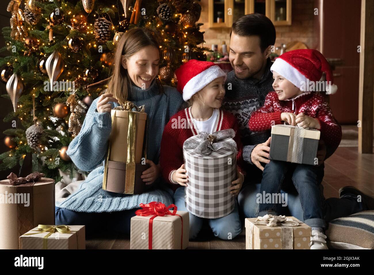 Smiling young family couple unwrapping Christmas gifts with kids Stock
