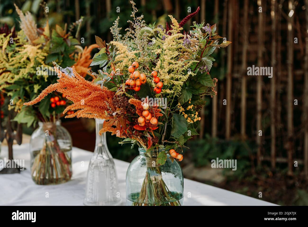 Rustic style. Boho style bouquets on the table in glass vases and jars. Wooden table and white tablecloth Stock Photo