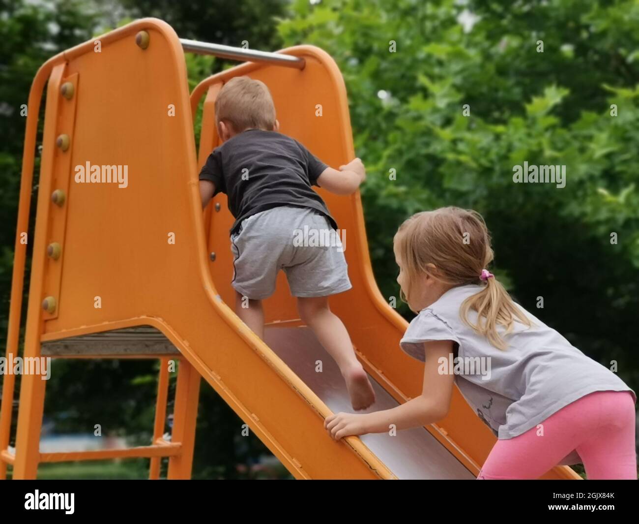 A Caucasian brother and a sister playing together in the playground ...