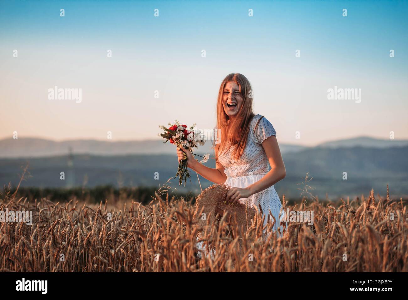 Portrait of young, teen, ginger girl with freckles in the wheat field, holding red bouquet. Copy space Stock Photo
