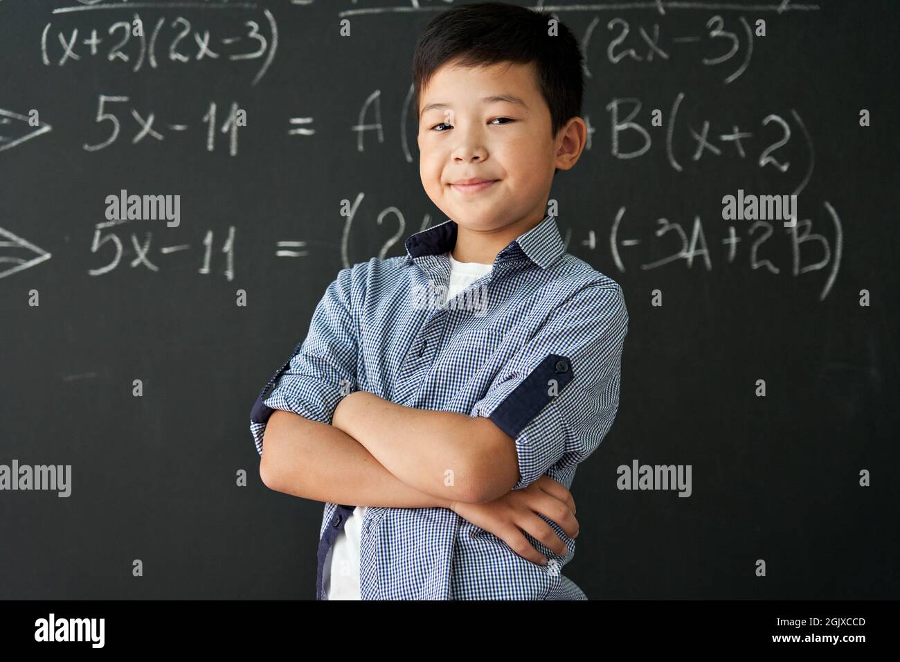 Portrait of happy proud asian boy standing on chalkboard background. Stock Photo