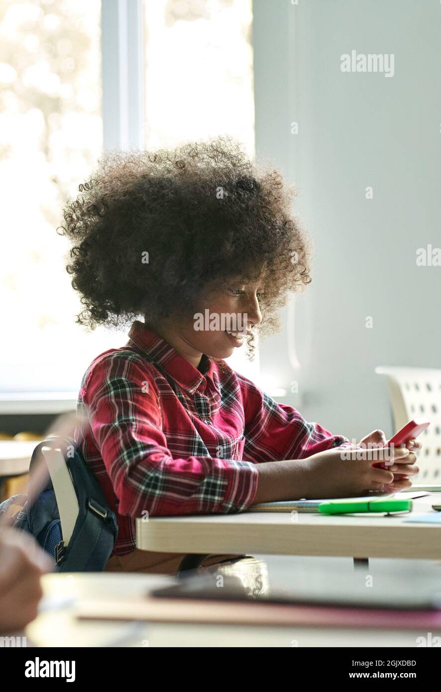 Happy smiling afro American schoolgirl using smartphone device in classroom. Stock Photo