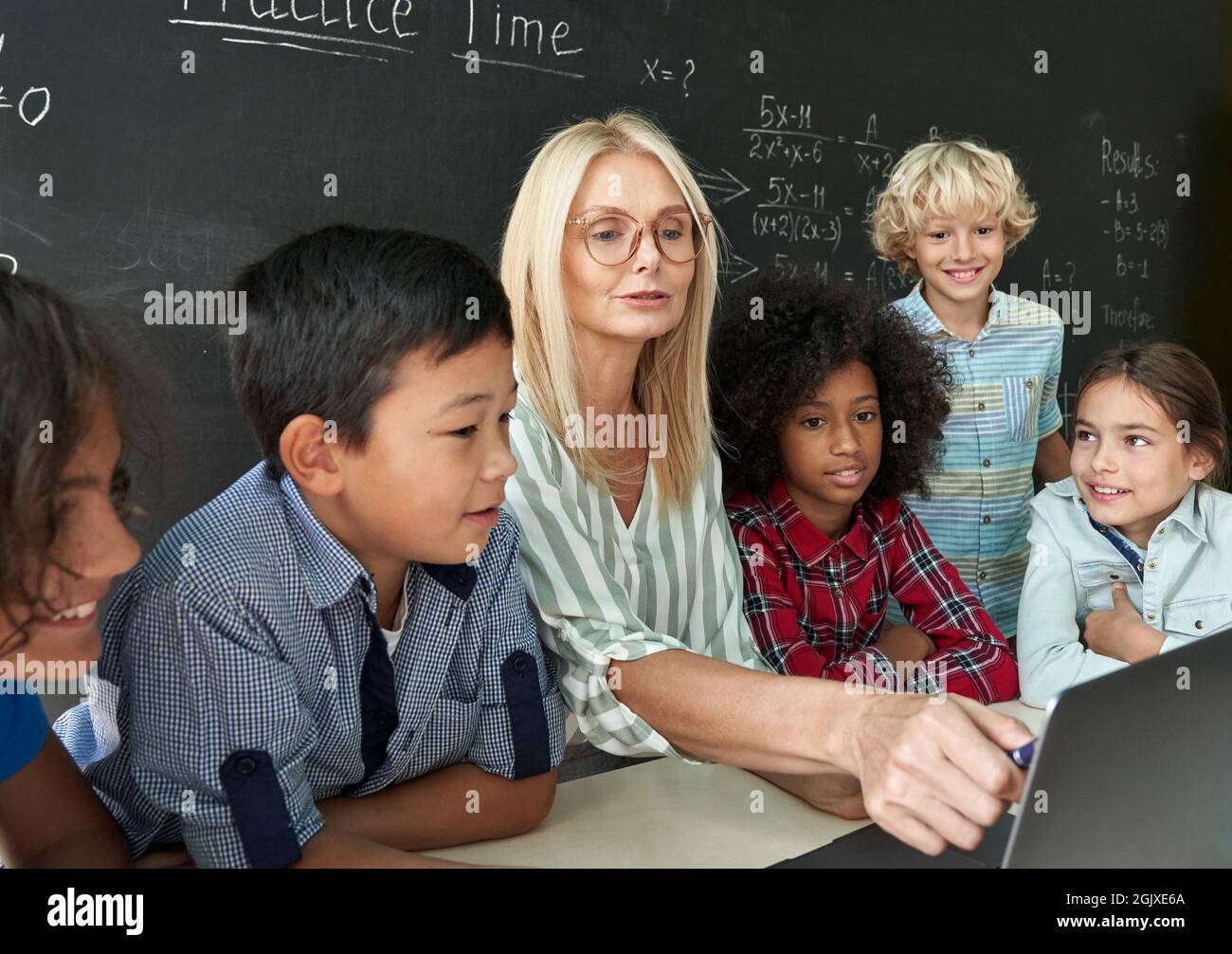 Happy teacher with diverse schoolkids having maths lesson sitting at desk. Stock Photo