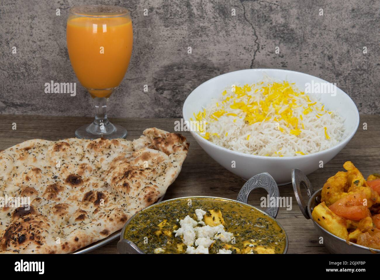 Garlic flavored naan bread from Indian restaurant part of huge table feast with mango lassi and sag paneer spinach bowl. Stock Photo