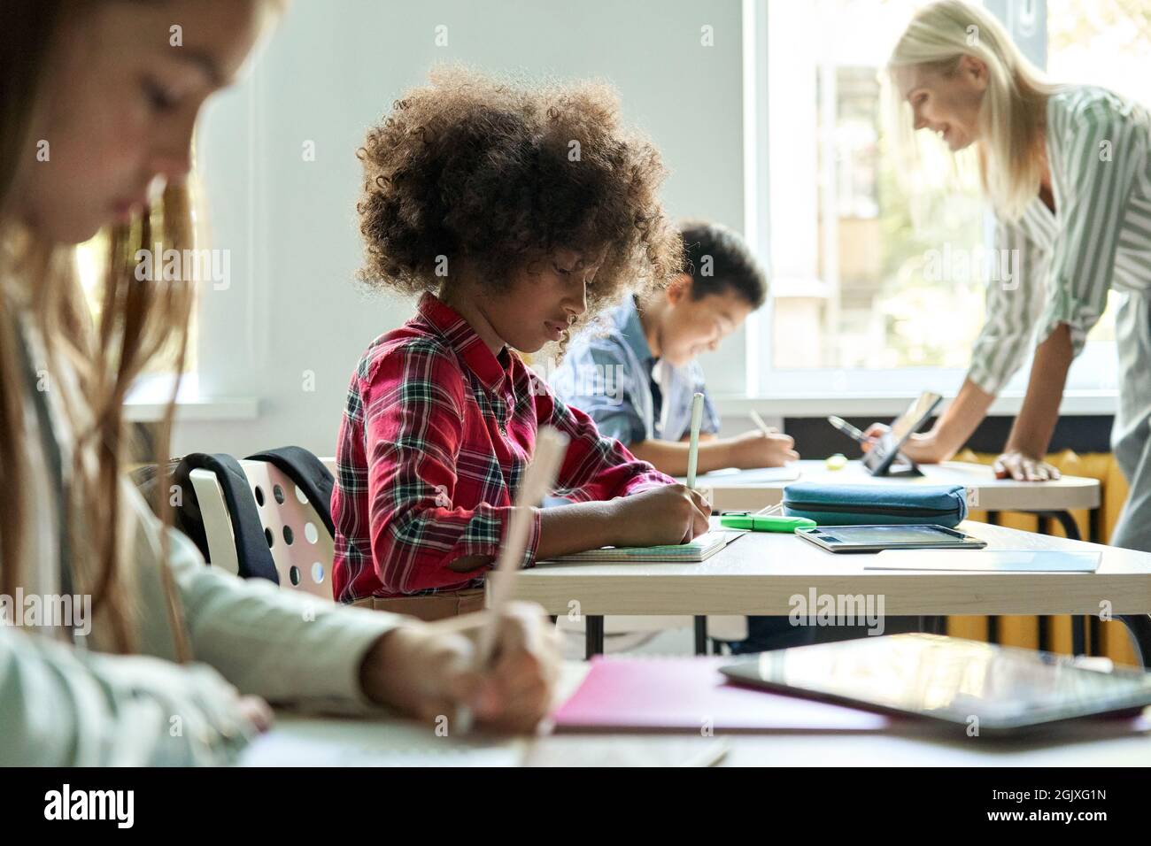 Diverse classmates doing task at lesson studying in classroom with teacher. Stock Photo