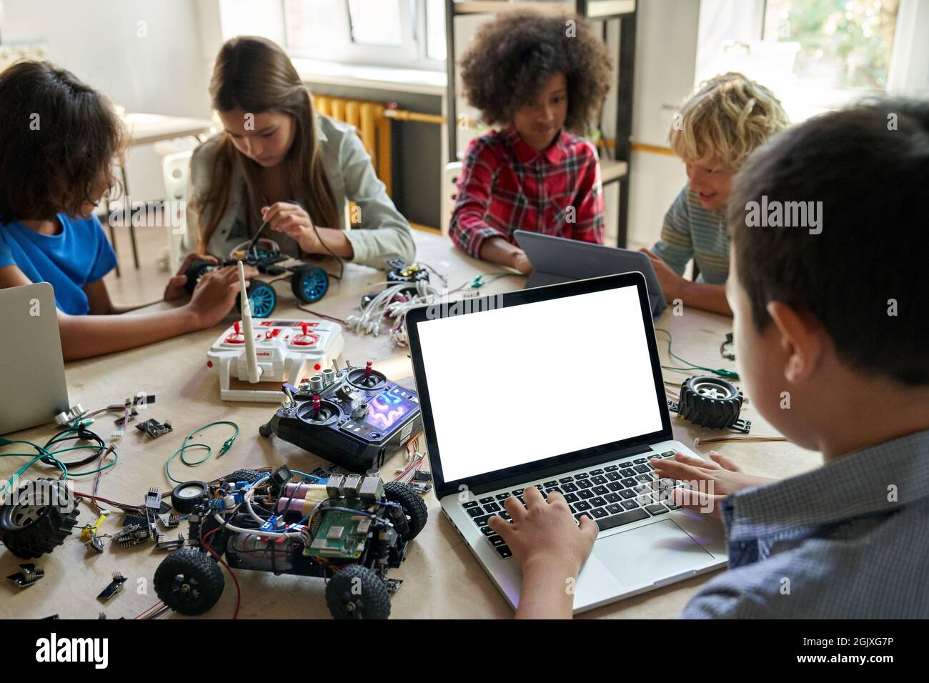 Diverse schoolkids at stem class building robot using pc with white screen. Stock Photo