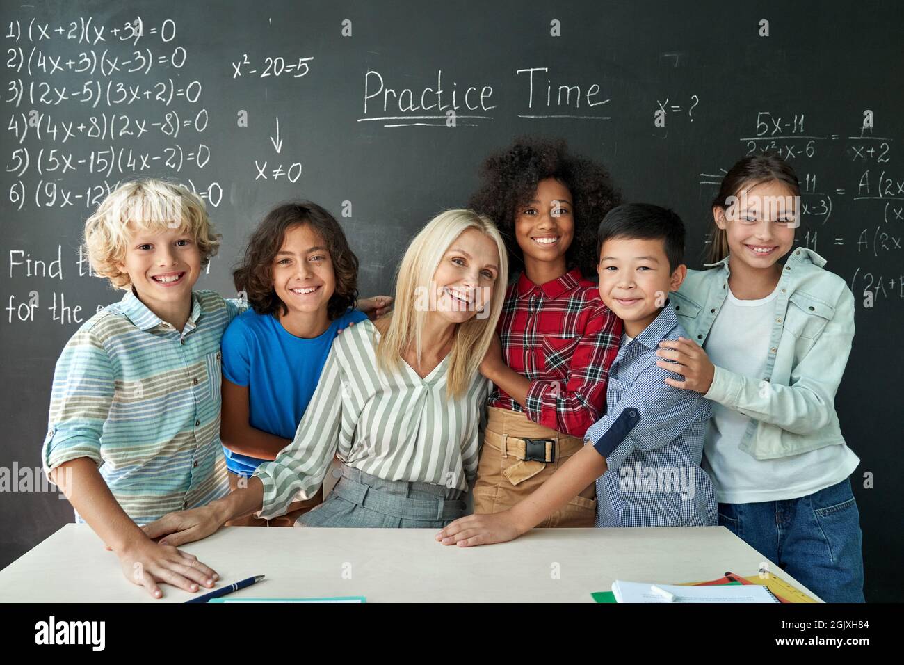 Portrait of cheerful smiling teacher and diverse schoolkids near chalkboard. Stock Photo