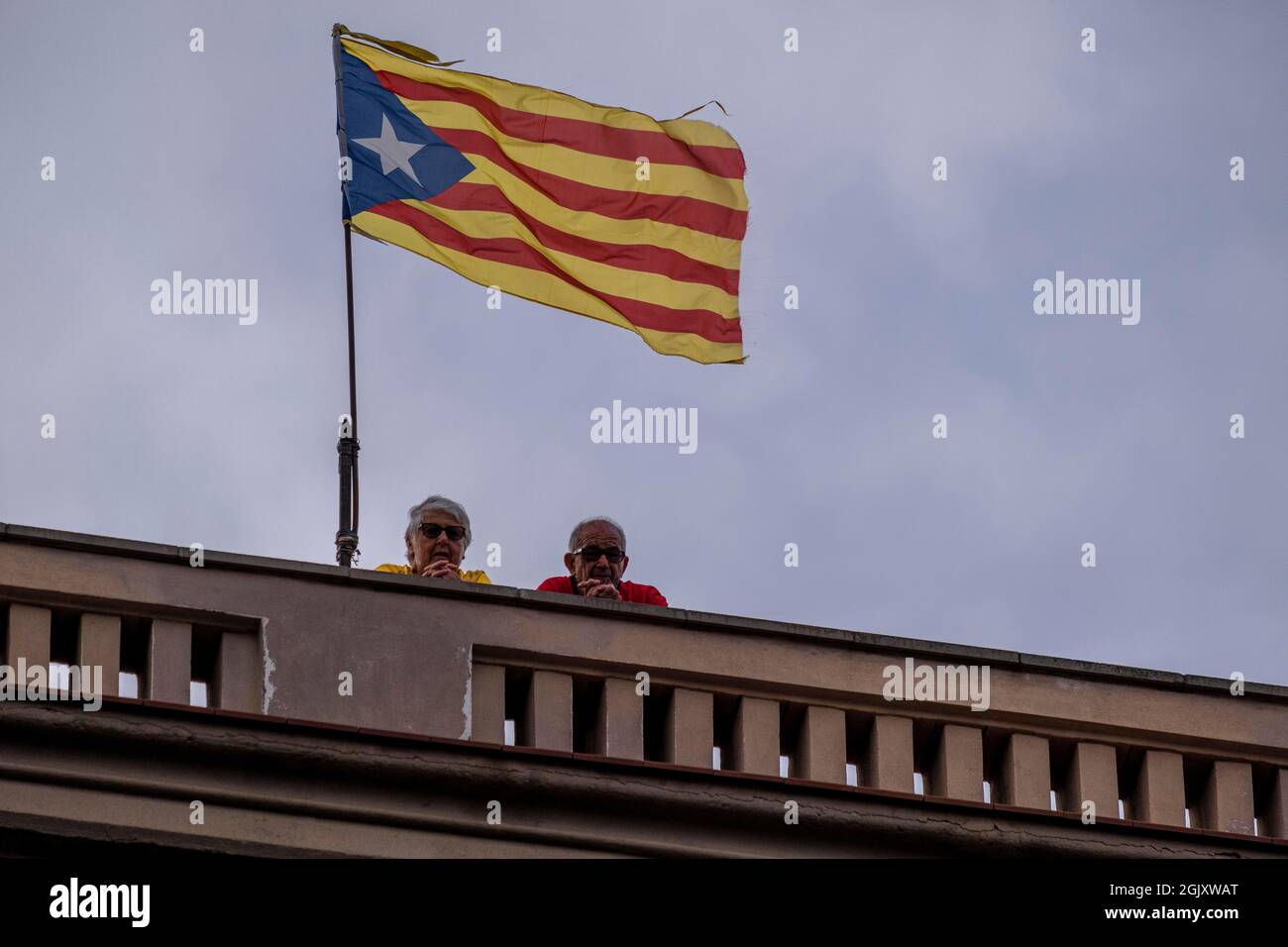Two people follow the act on the stage of Avenida Marquès de l'Argentera from the terrace of an adjoining building with a pro-independence flag raised.According to figures from the organizers, there are around 400,000 people, according to the Guàrdia Urbana, a little more than 100,000 who convened under the slogan 'Lluitem i Guanyem la indepència' (let's fight and win Independence) have attended the unitary demonstration to celebrate September 11, Diada of Catalonia. Stock Photo