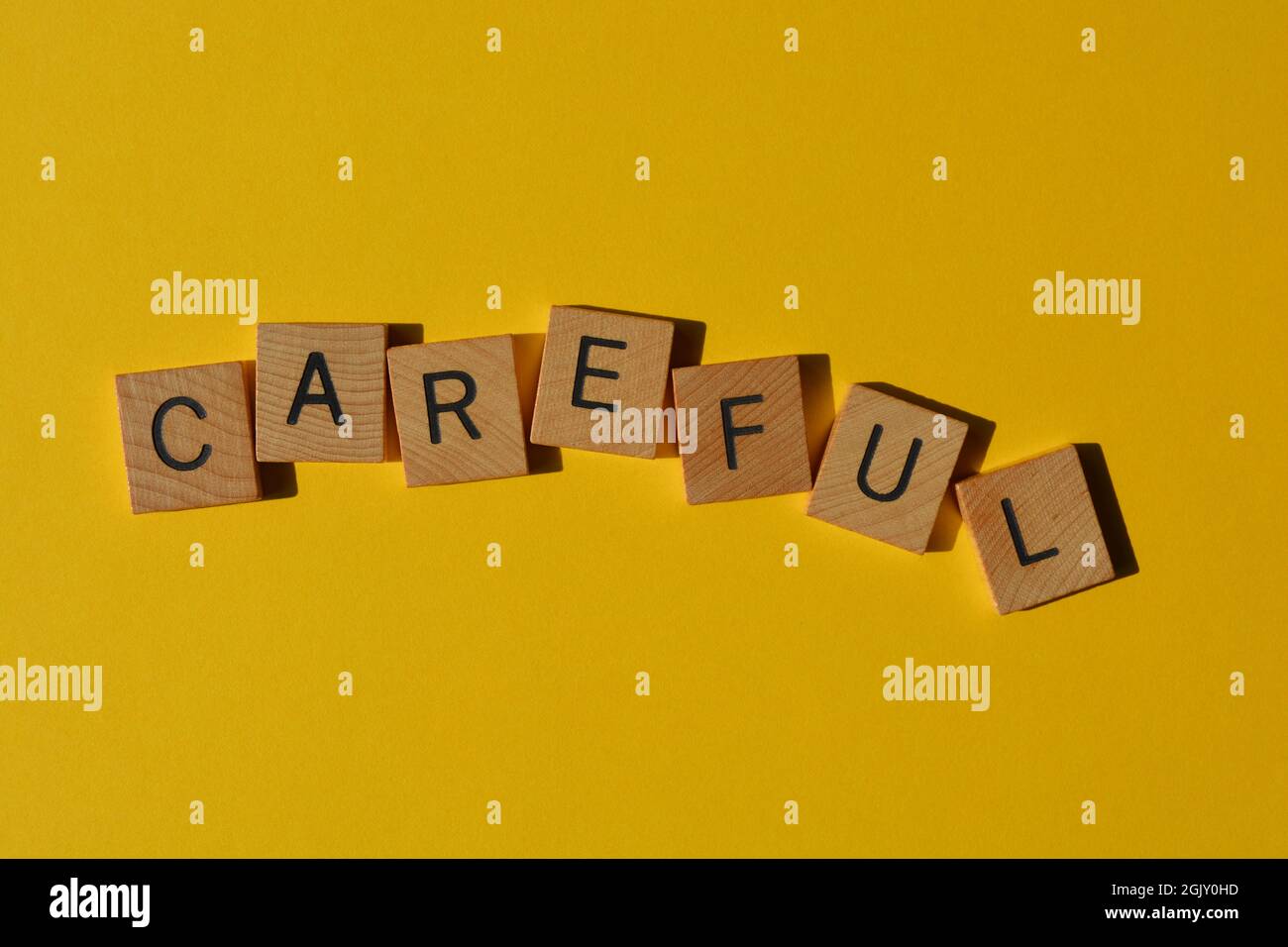 Careful, word in wooden alphabet letters isolated on yellow background  with copy space Stock Photo