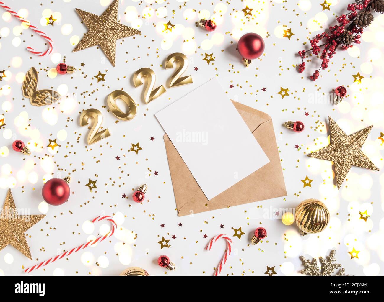 Open brown envelope with blank white card and numbers of 2022 for the coming year and festive seasonal decorations on white background. Top view. Stock Photo