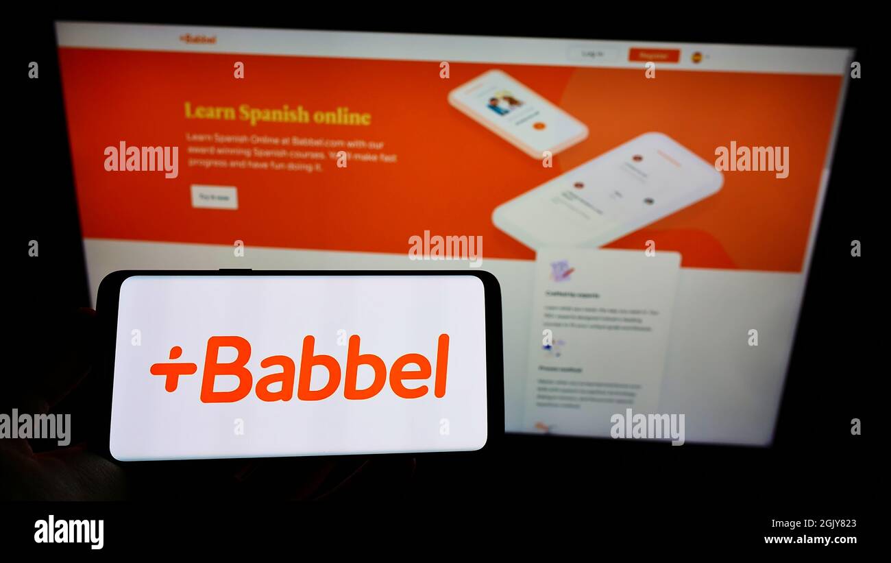 Person holding mobile phone with logo of German language learning company Babbel GmbH on screen in front of web page. Focus on phone display. Stock Photo