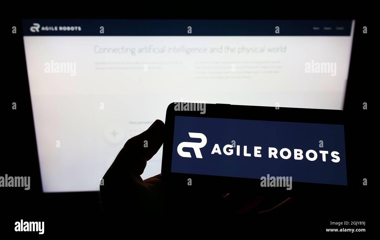 Person holding smartphone with logo of German technology company Agile Robots AG on screen in front of website. Focus on phone display. Stock Photo