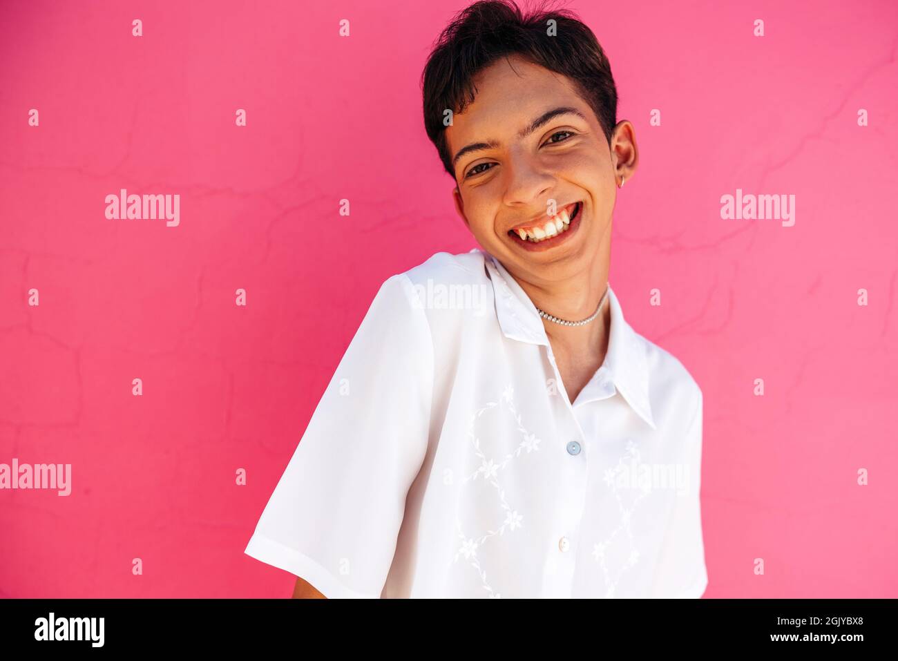 Young teenage boy feeling proud of his queer identity. Happy gay teenager smiling at the camera cheerfully. Carefree young teenage boy standing agains Stock Photo