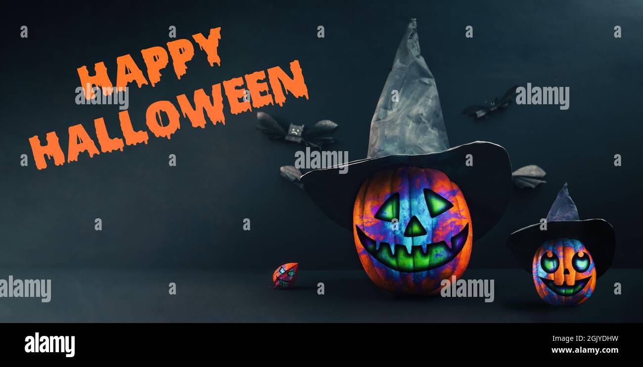 Happy Halloween banner with Jack-o-lanterns. Two decorated multicolored pumpkin in a black witch's hat with physalis and bats made of paper. Dark back Stock Photo