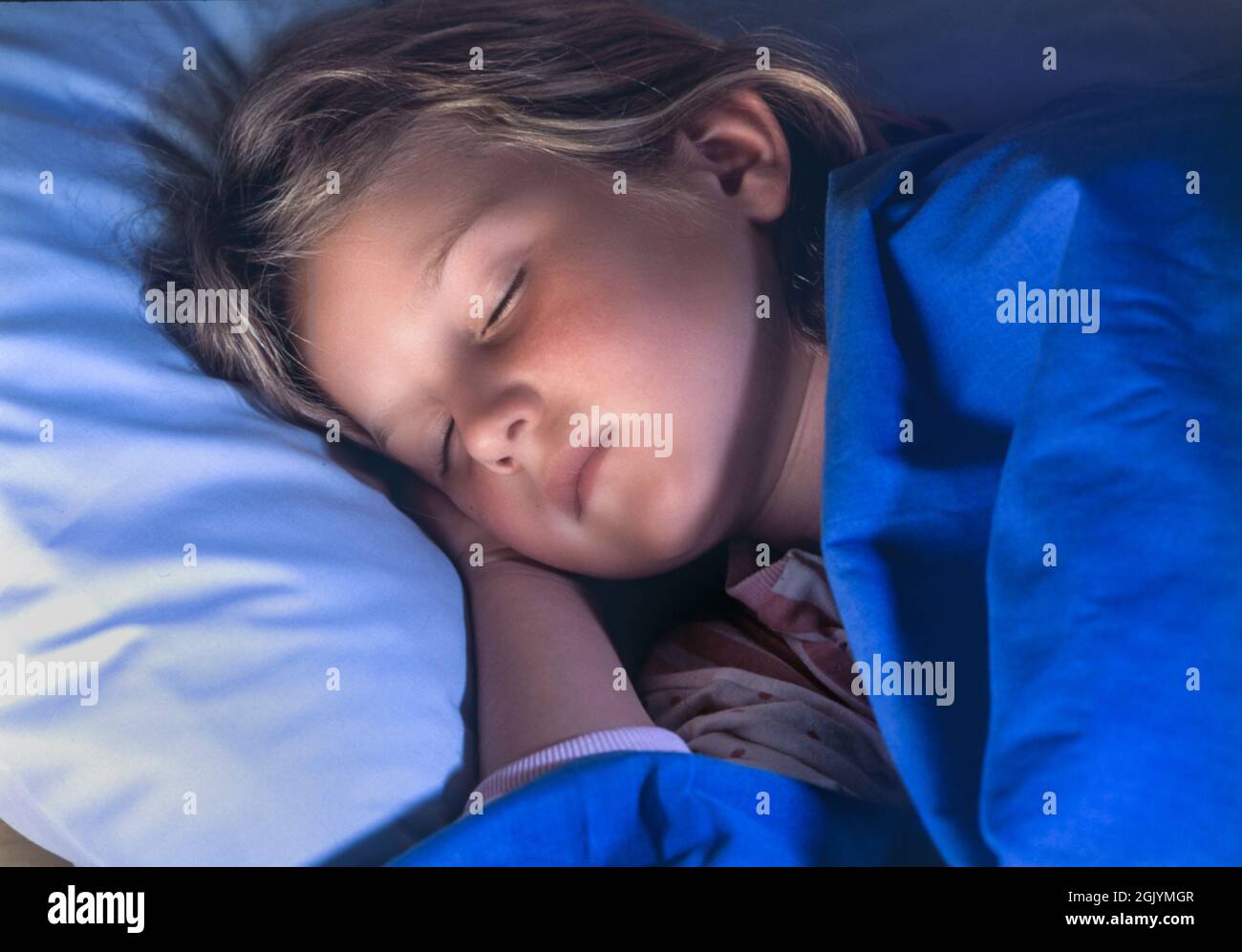 Sleeping asleep face rest young girl 6-8 years asleep with head on pillow in bed peacefully resting, in night time bed bedroom, secure healthy sleep in comfortable family home situation Stock Photo