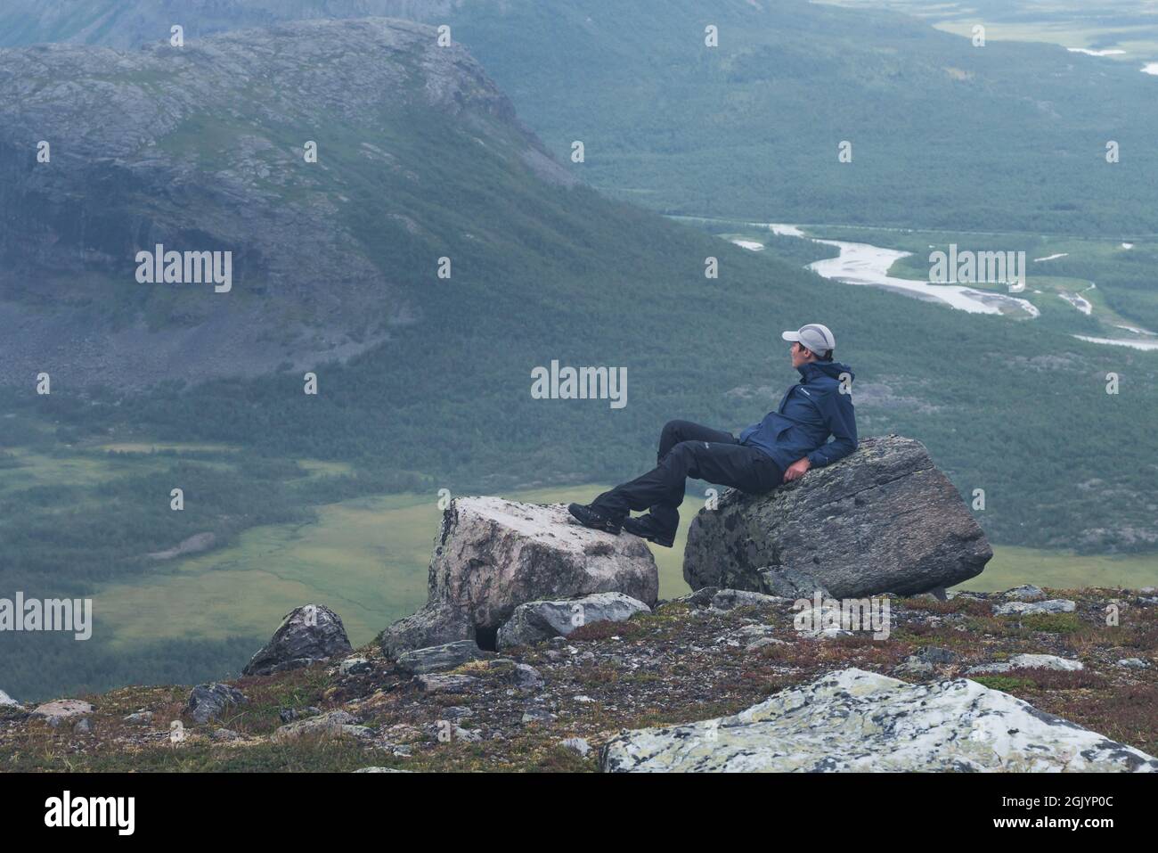Female hiker in blue jacket overlooking remote arctic valley on a cloudy day of arctic summer. Hiking in Sarek National Park, Sweden, with Rapa River Stock Photo