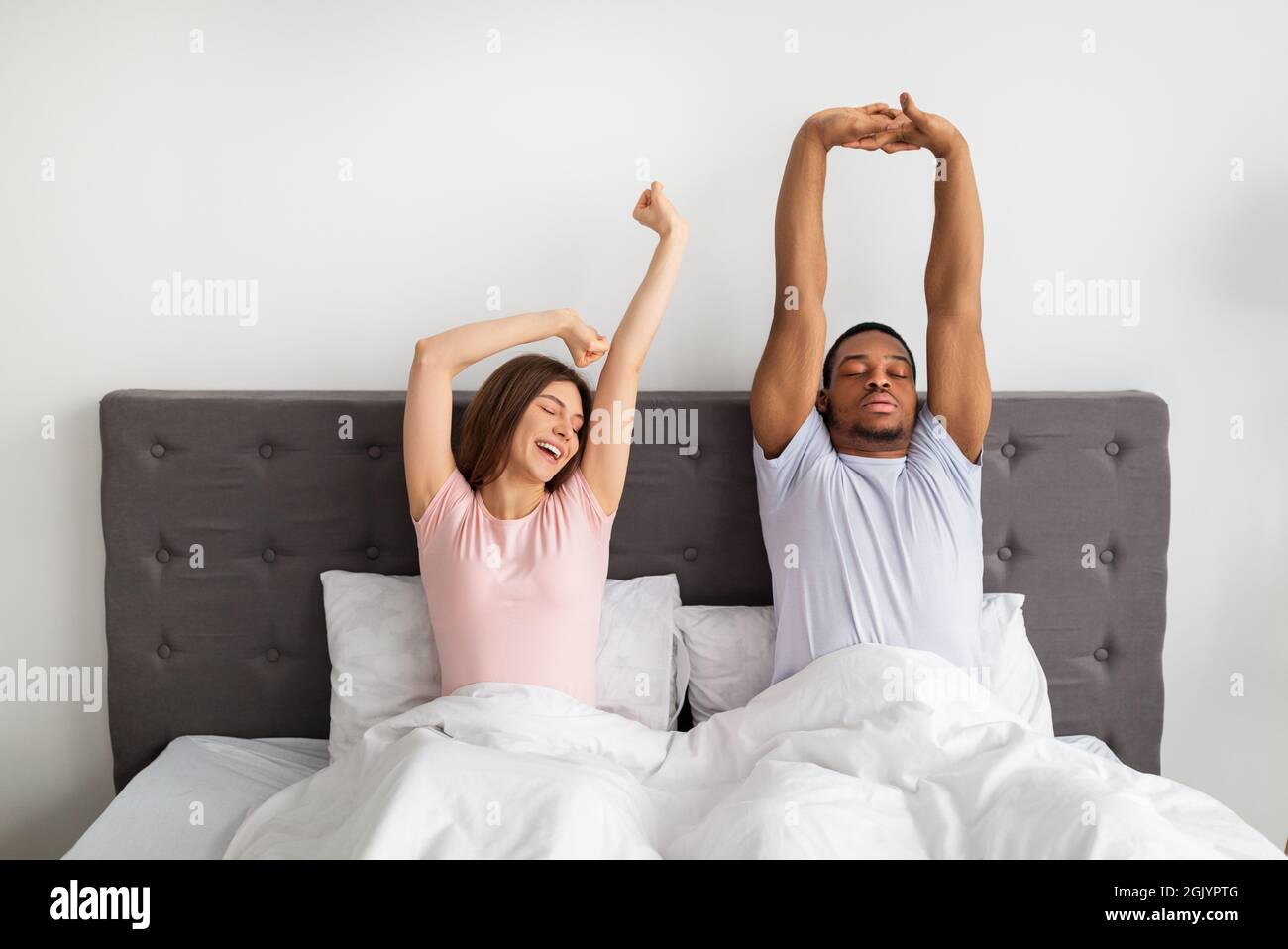 Multinational couple stretching on bed after waking up, feeling sleepy at home Stock Photo