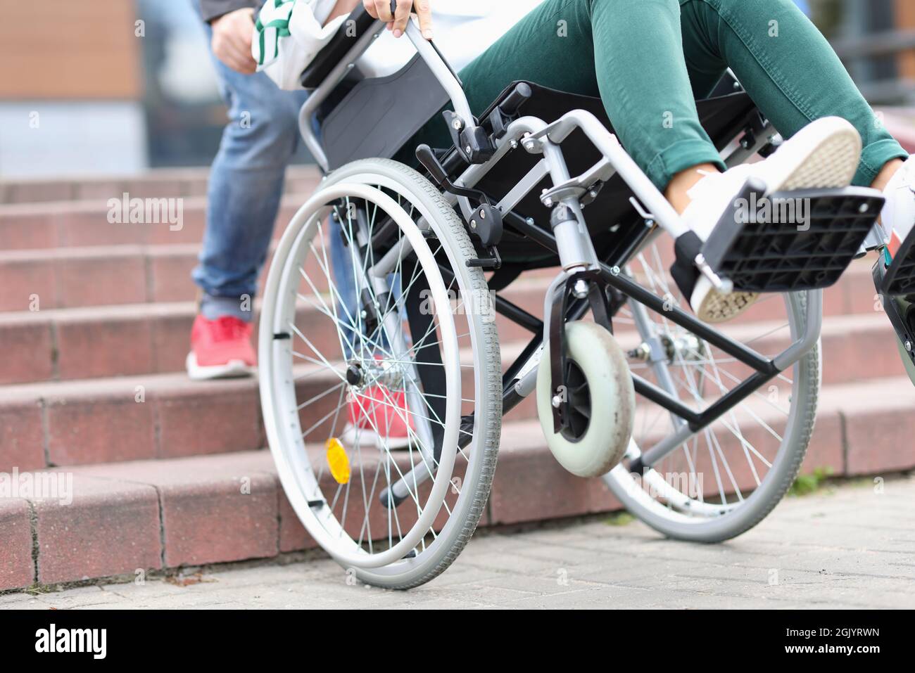 Man pulling disabled woman in wheelchair up steps closeup Stock Photo
