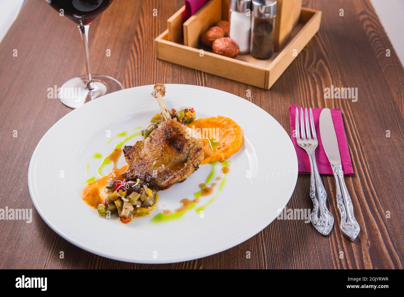 Duck leg confit, served on a pillow of pumpkin puree and salad as a delicious meat food dish for dinner. Served with red wine Stock Photo