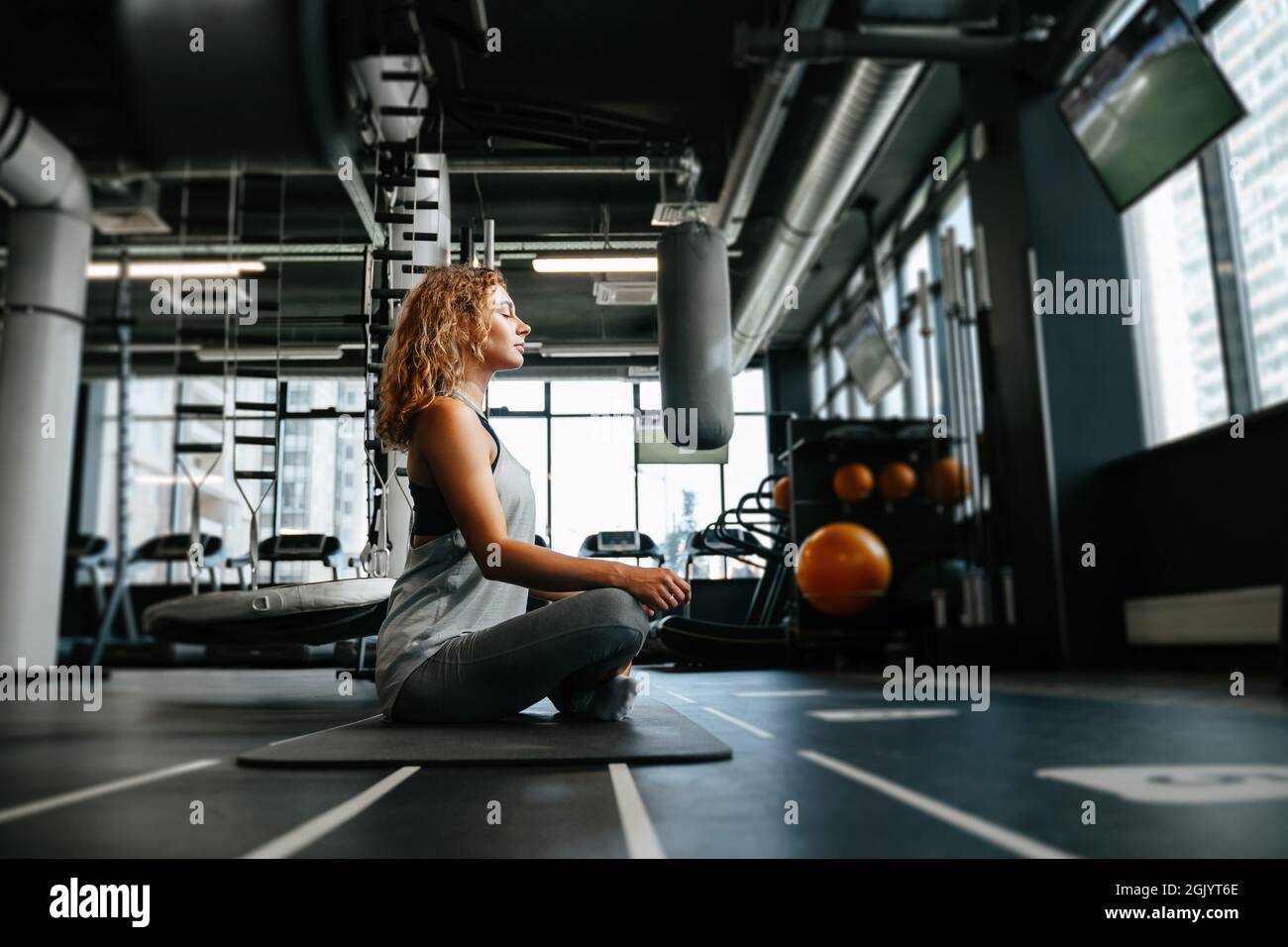 Young woman is doing yoga in the gym sitting on the floor in the lotus ...
