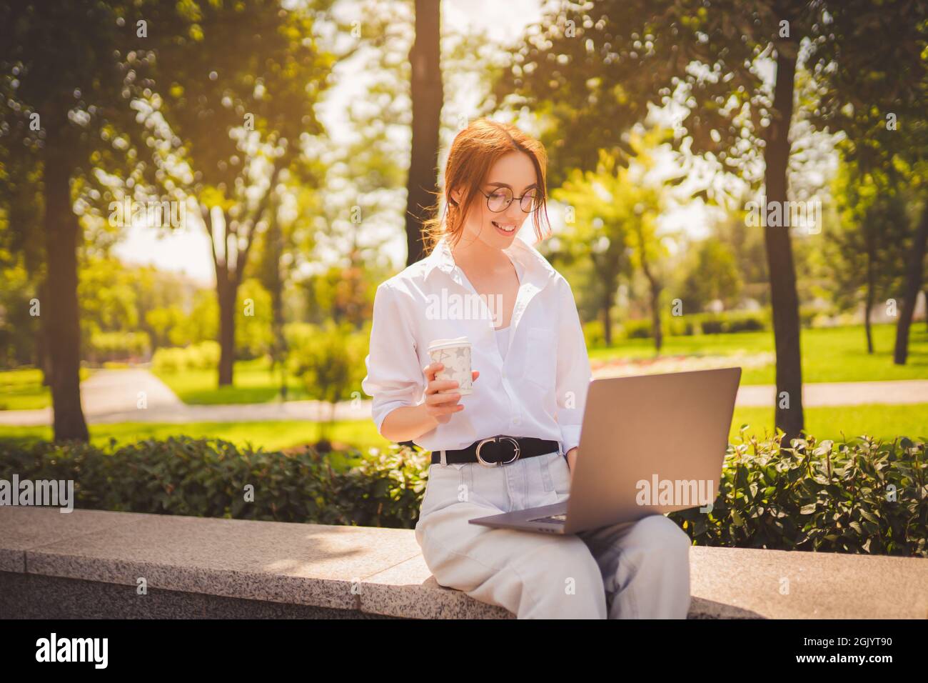 Beautiful redhead young woman sitting in the park and using laptop ...