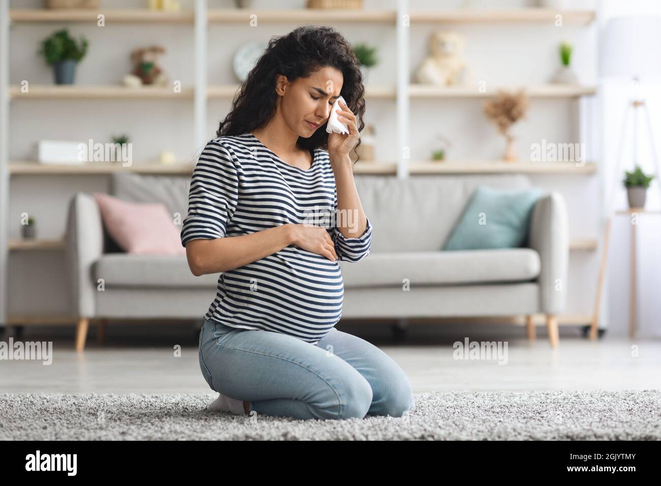 Crying pregnant woman feeling down while staying alone at home Stock Photo