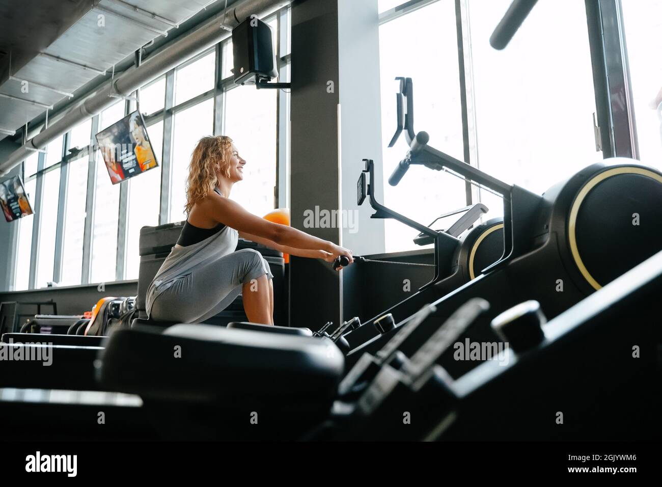 Athletic woman is engaged in rowing in the gym for muscle training. Stock Photo