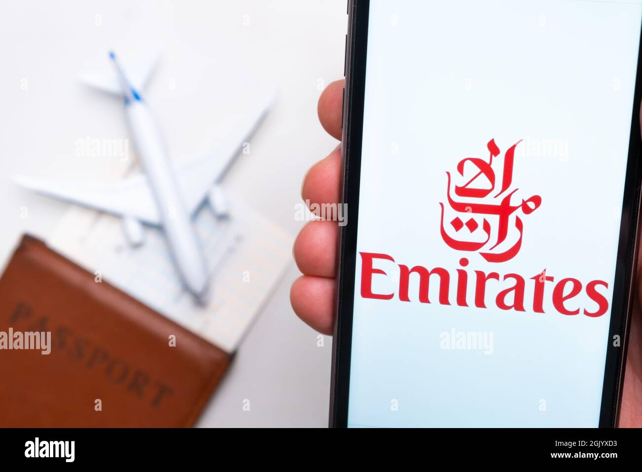 Emirates airline company logo on the screen of mobile phone in man hand on the background of passport, boarding pass and plane, September 2021, San Stock Photo
