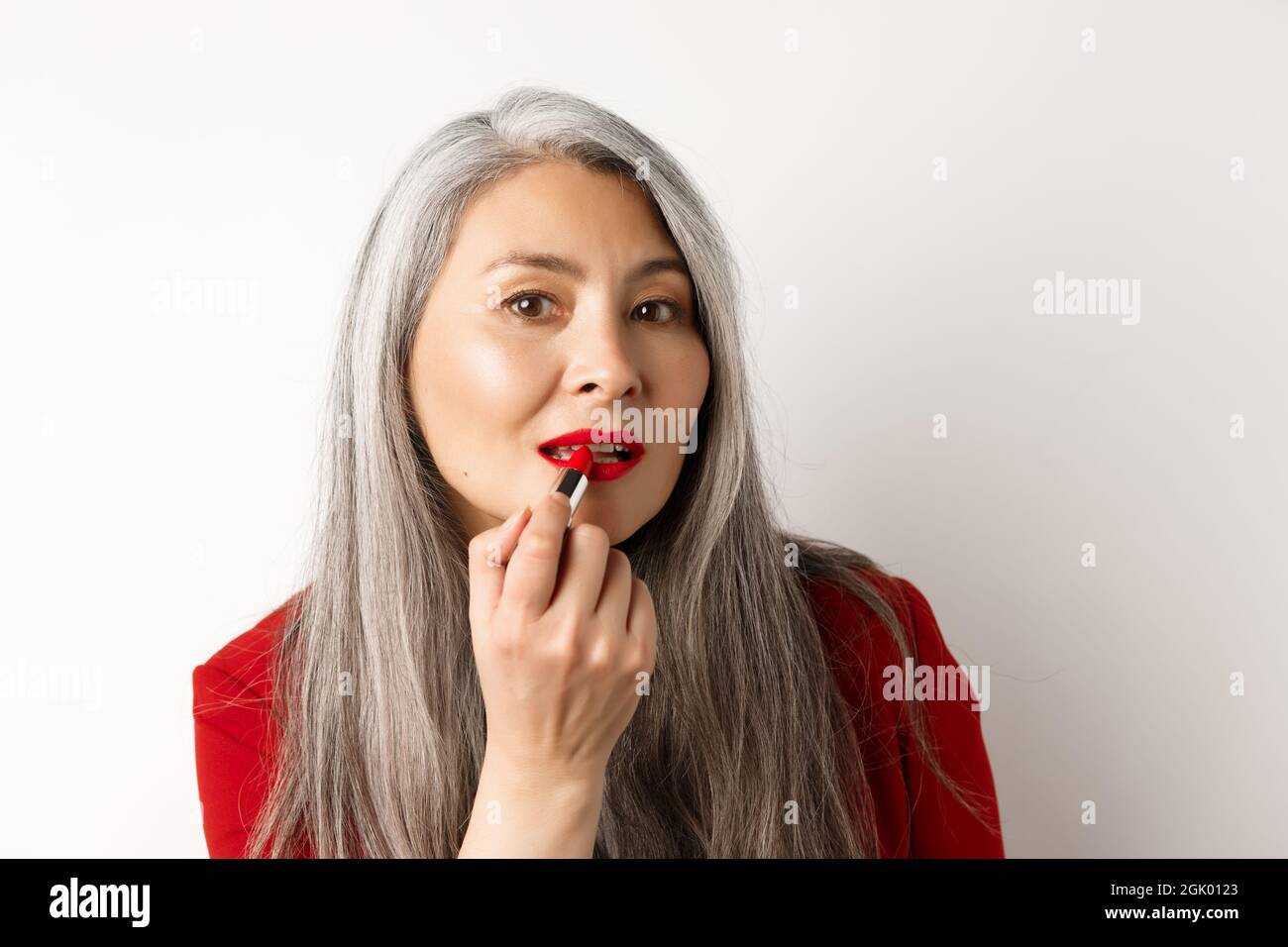 Beauty and makeup concept. Stylish asian mature woman with grey hair,  looking in mirror and apply red lipstick, standing over white background  Stock Photo - Alamy