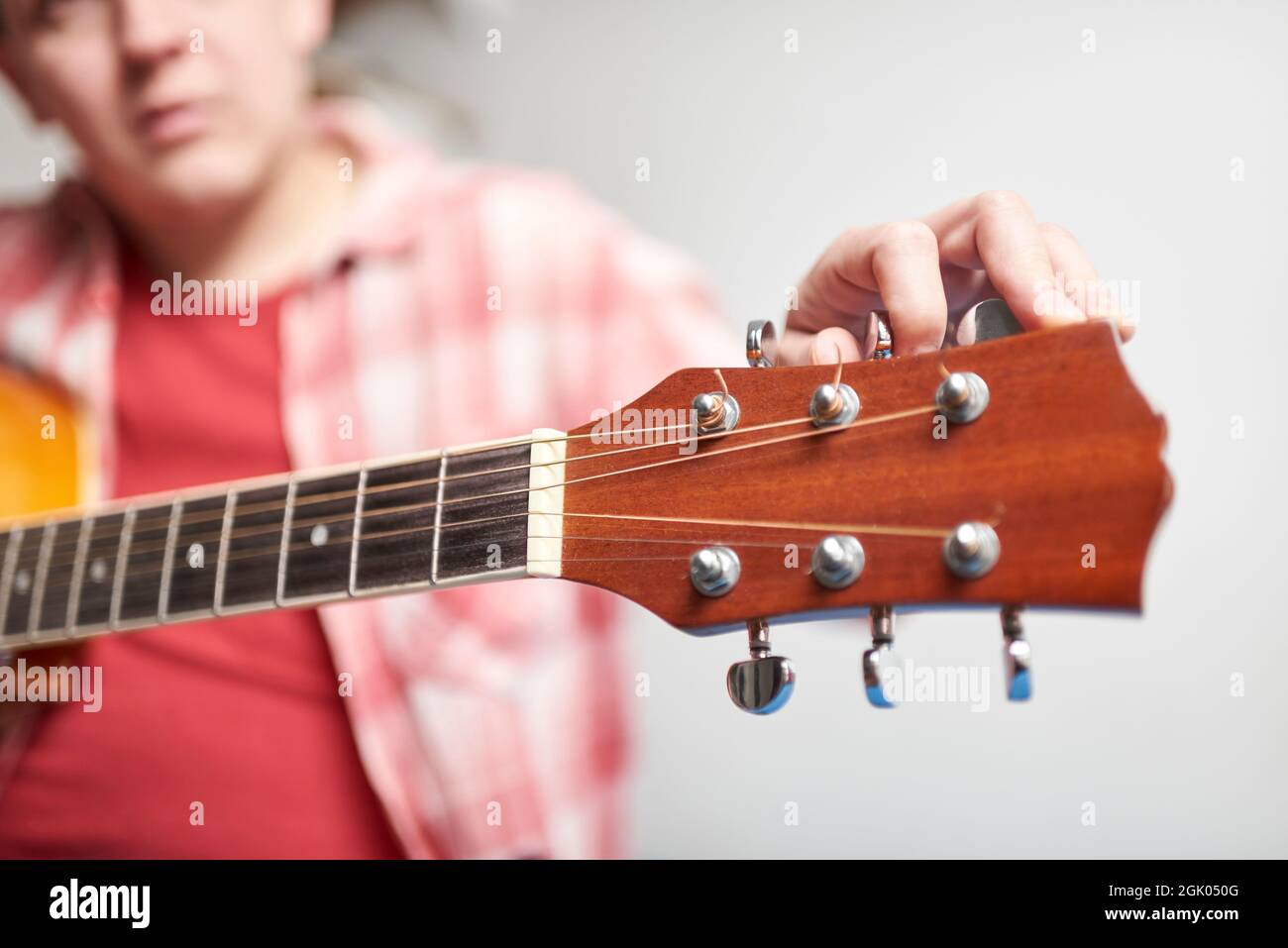 Young unknown man tuning a guitar, detail shot, focus in the hand and the headstock. Stock Photo