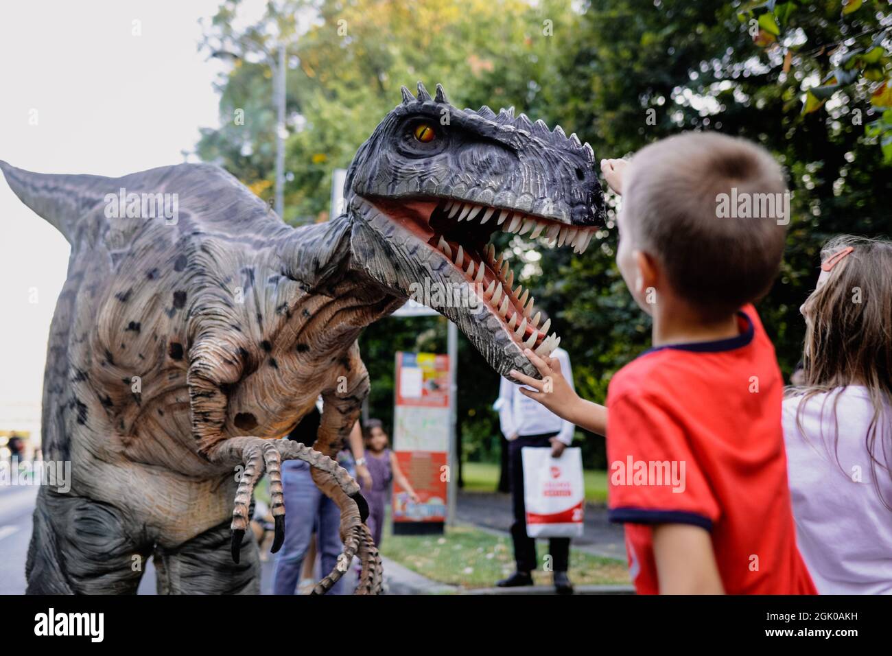 Bucharest, Romania - August 29, 2021: A man costumed as a carnivorous dinosaur walks between people and let’s them pet him during an outdoors event in Stock Photo