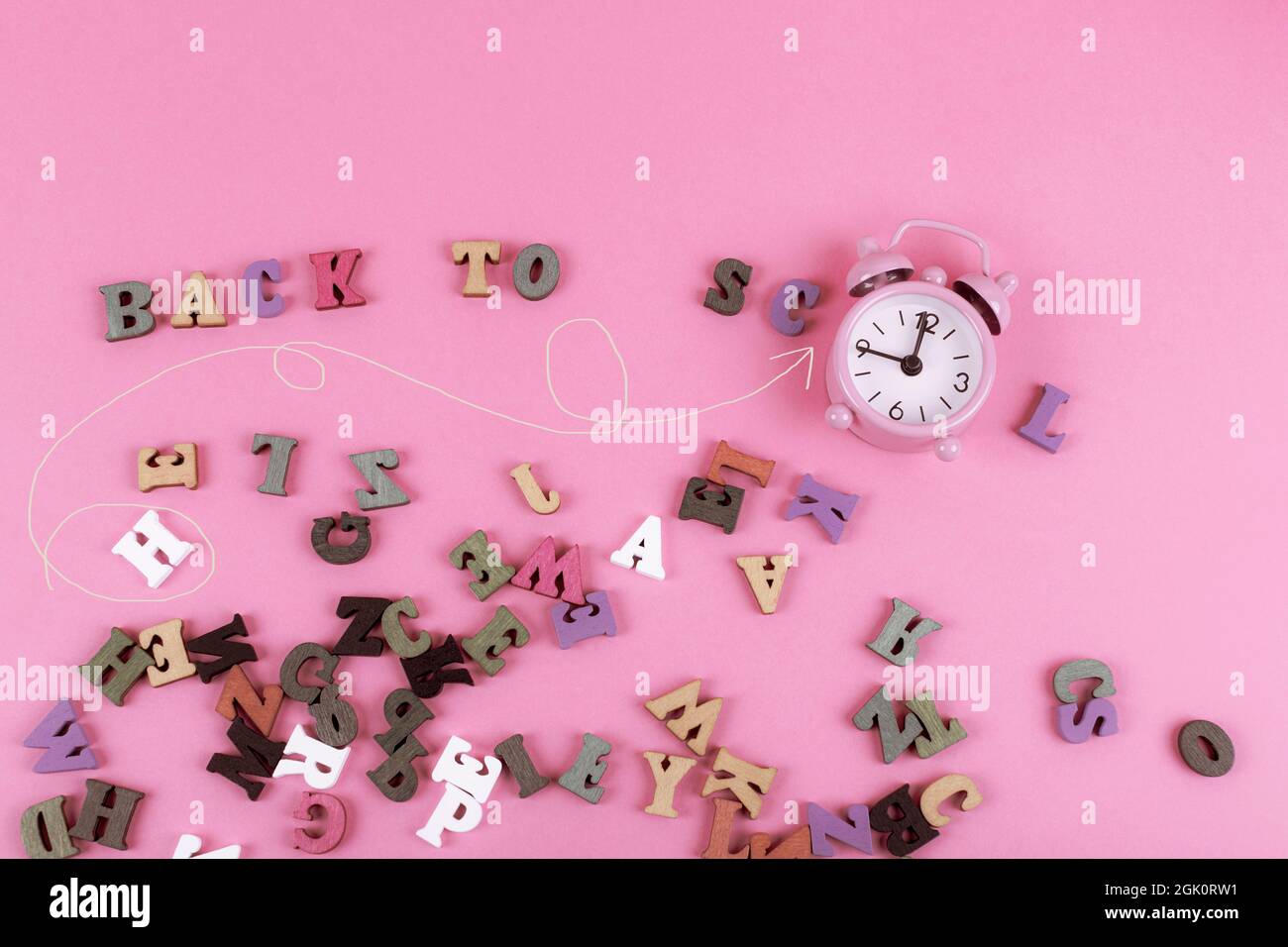 Pink alarm clock with scattered letters on a pink background. Back to ...