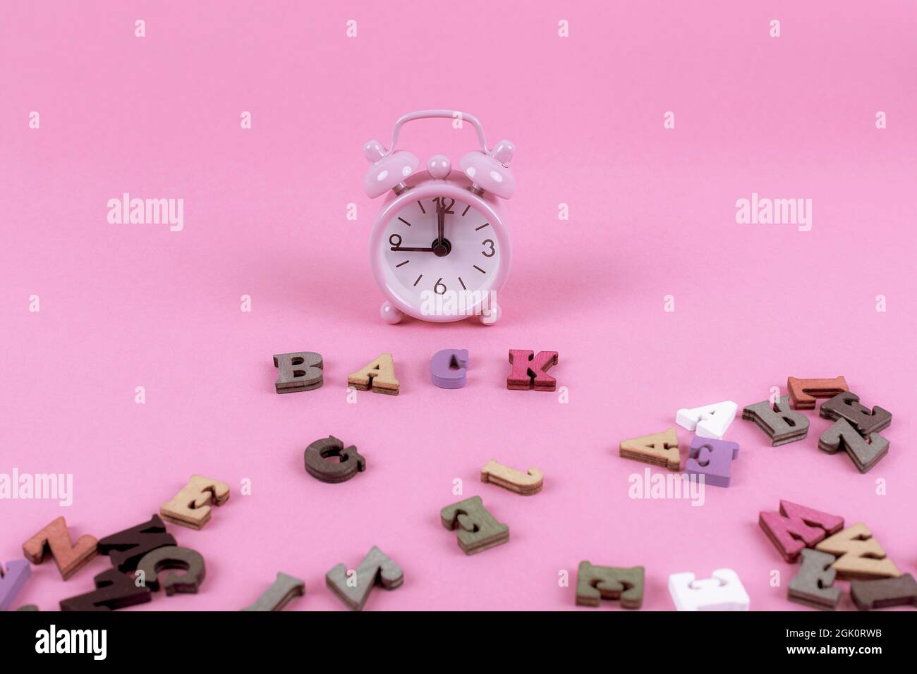 Pink alarm clock with scattered letters on a pink background. Back to ...