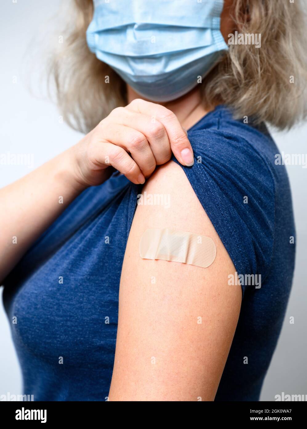 Vaccinated young woman showing arm with plaster, female person in mask after getting COVID-19 vaccine. Concept of people corona virus vaccination, inj Stock Photo