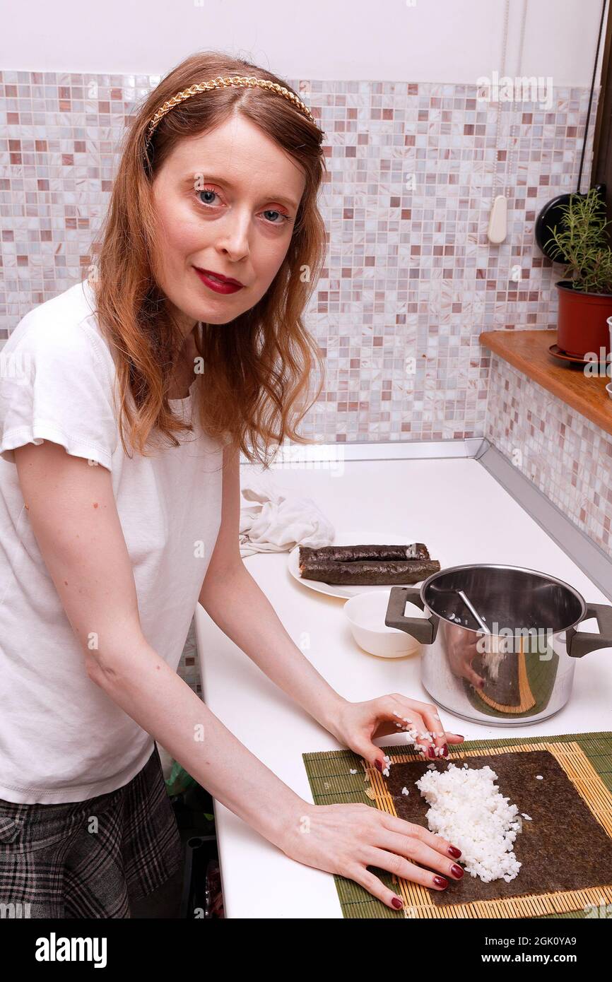 Young woman using bamboo rolling mat to make homemade sushi with salmon