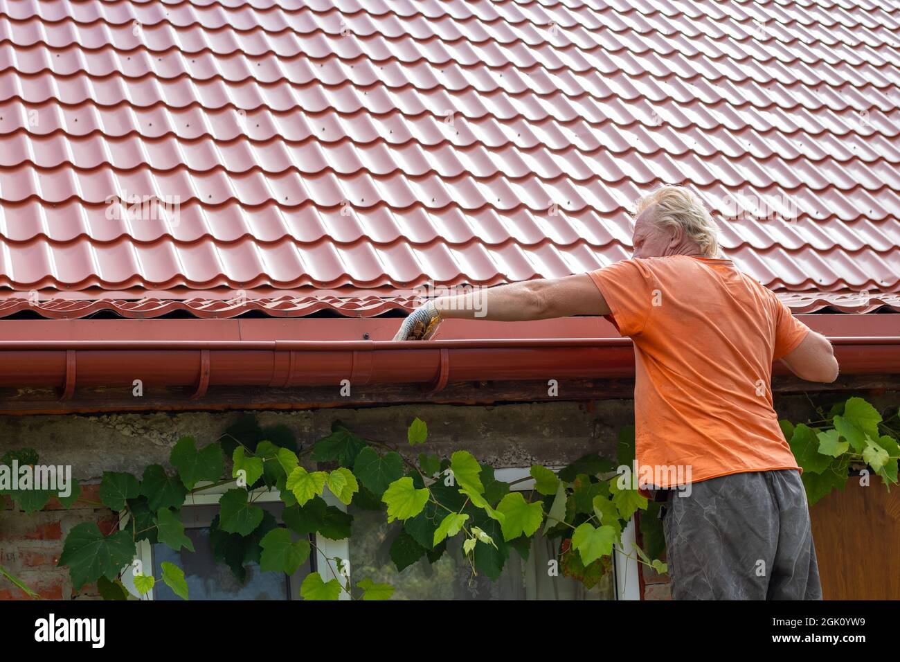 A man cleans out debris and leaves from the gutter system on the roof ...