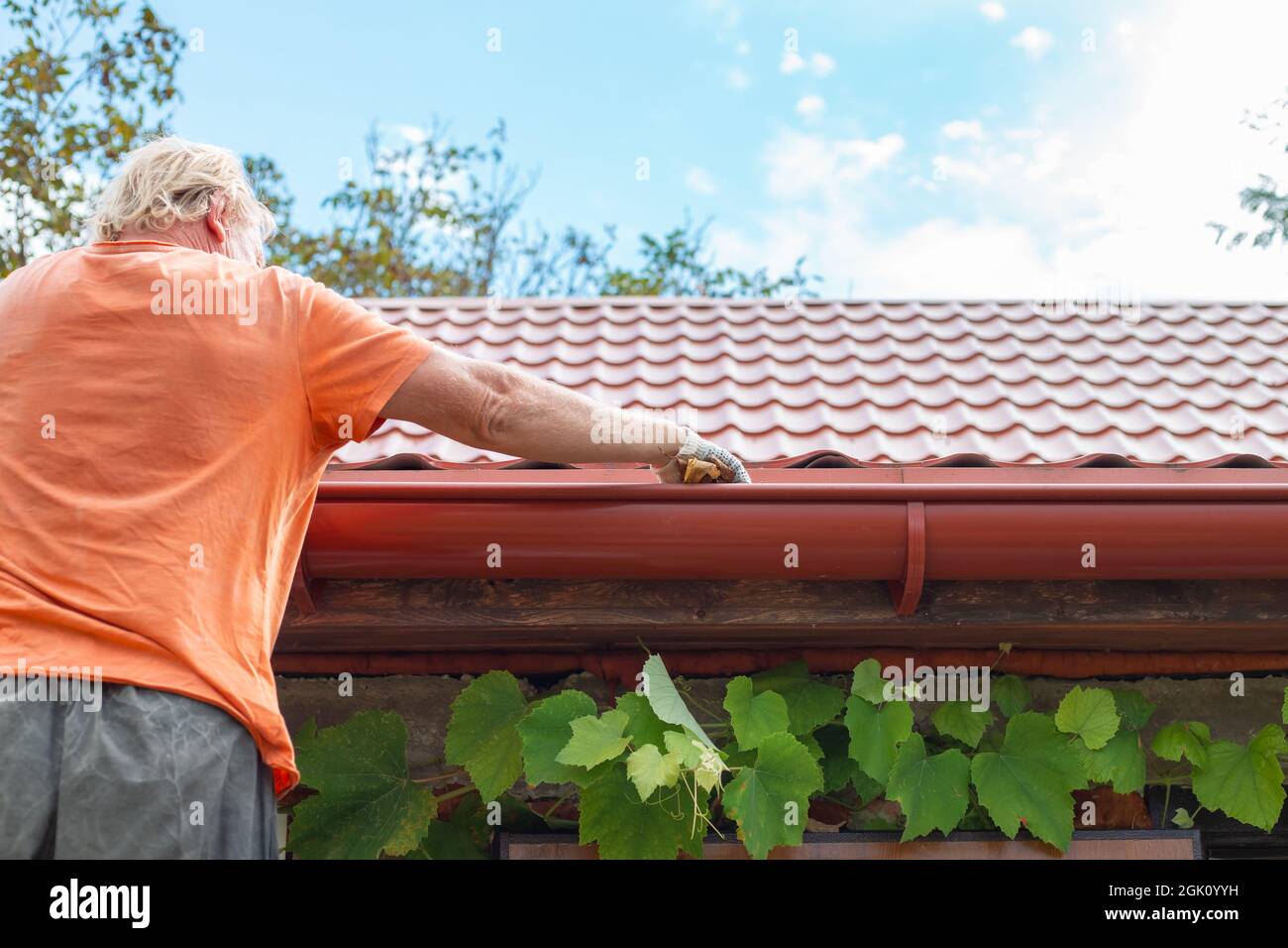 A man cleans out debris and leaves from the gutter system on the roof ...
