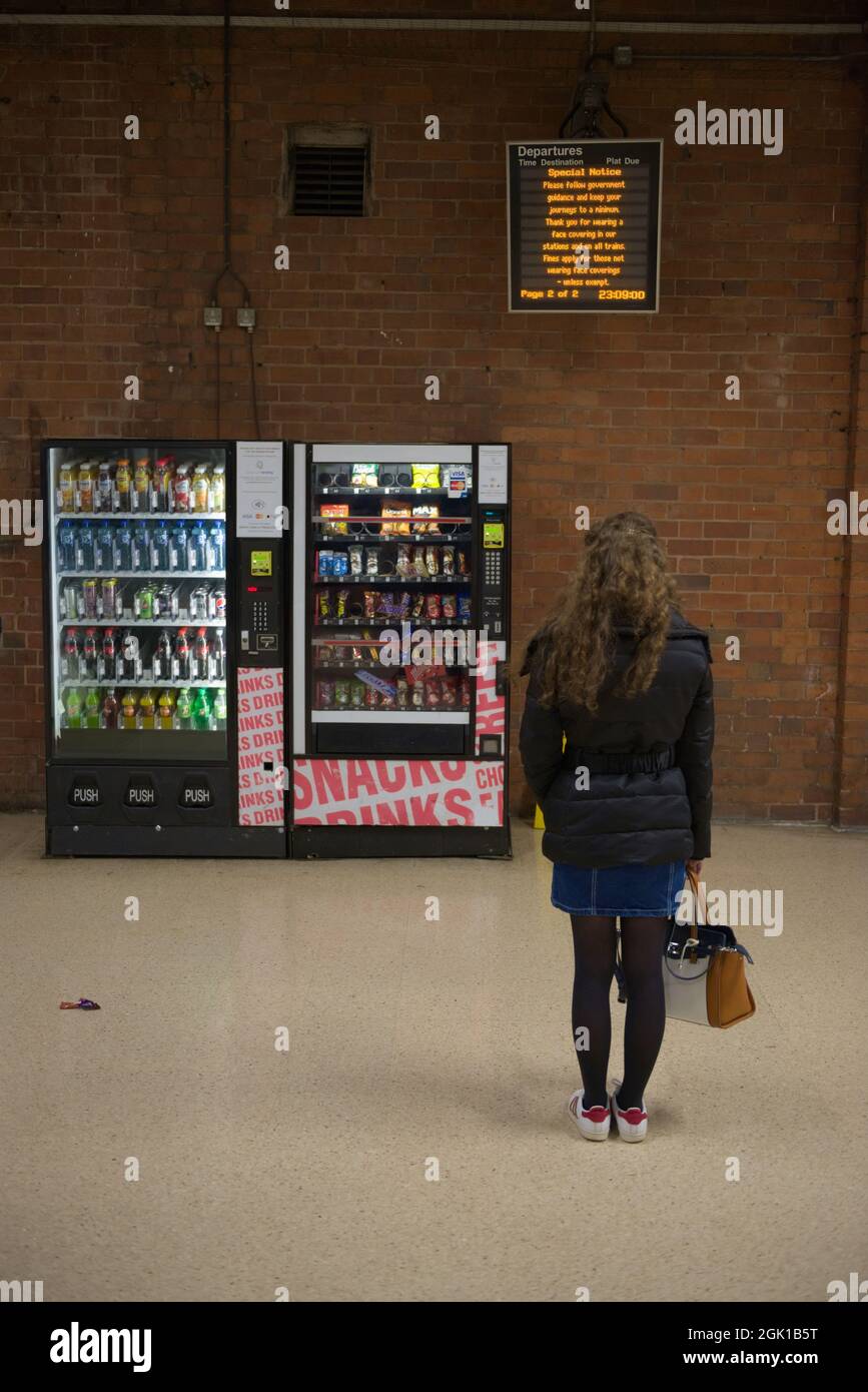 Doncaster, United Kingdom, 22nd May, 2021: Departure board displays COVID information for rail travel, read by a young woman stood by vending machines Stock Photo