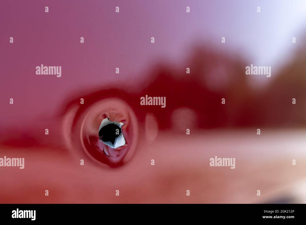 Close up shot of a bullet hole on within the passenger side door of a red car. Stock Photo