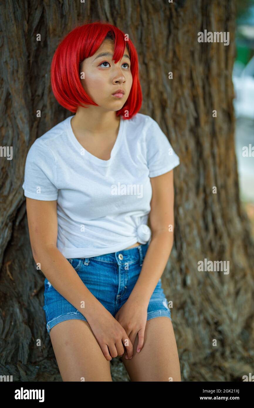 Red Blood Cell Cosplay Actress Standing with Redwood Tree | Teen Asian Girl with Red Wig Stock Photo