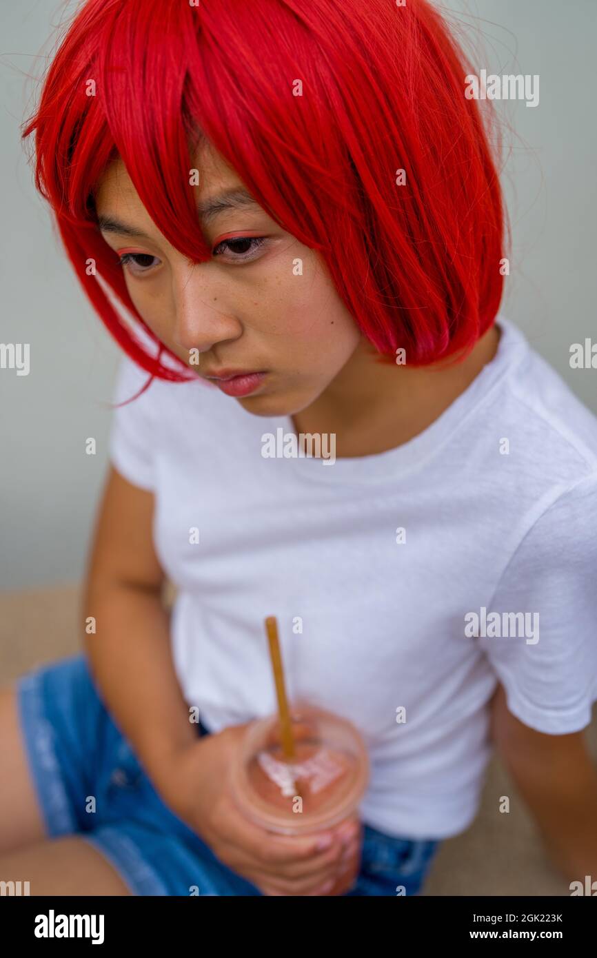 Red Blood Cell Cosplay Actress Seated Drinking a Smoothie | Asian Teenage Girl in Red Wig Stock Photo