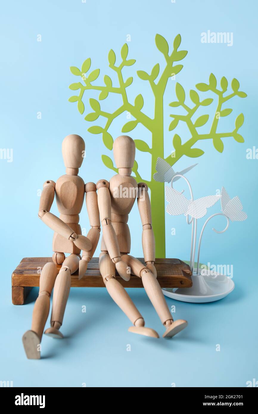 Wooden mannequins sitting on bench on color background Stock Photo - Alamy