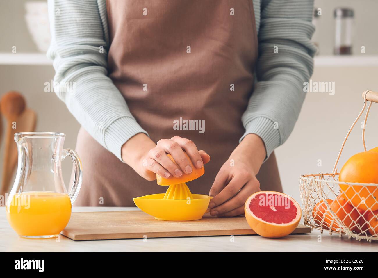 Woman squeezing grapefruit on table in kitchen Stock Photo