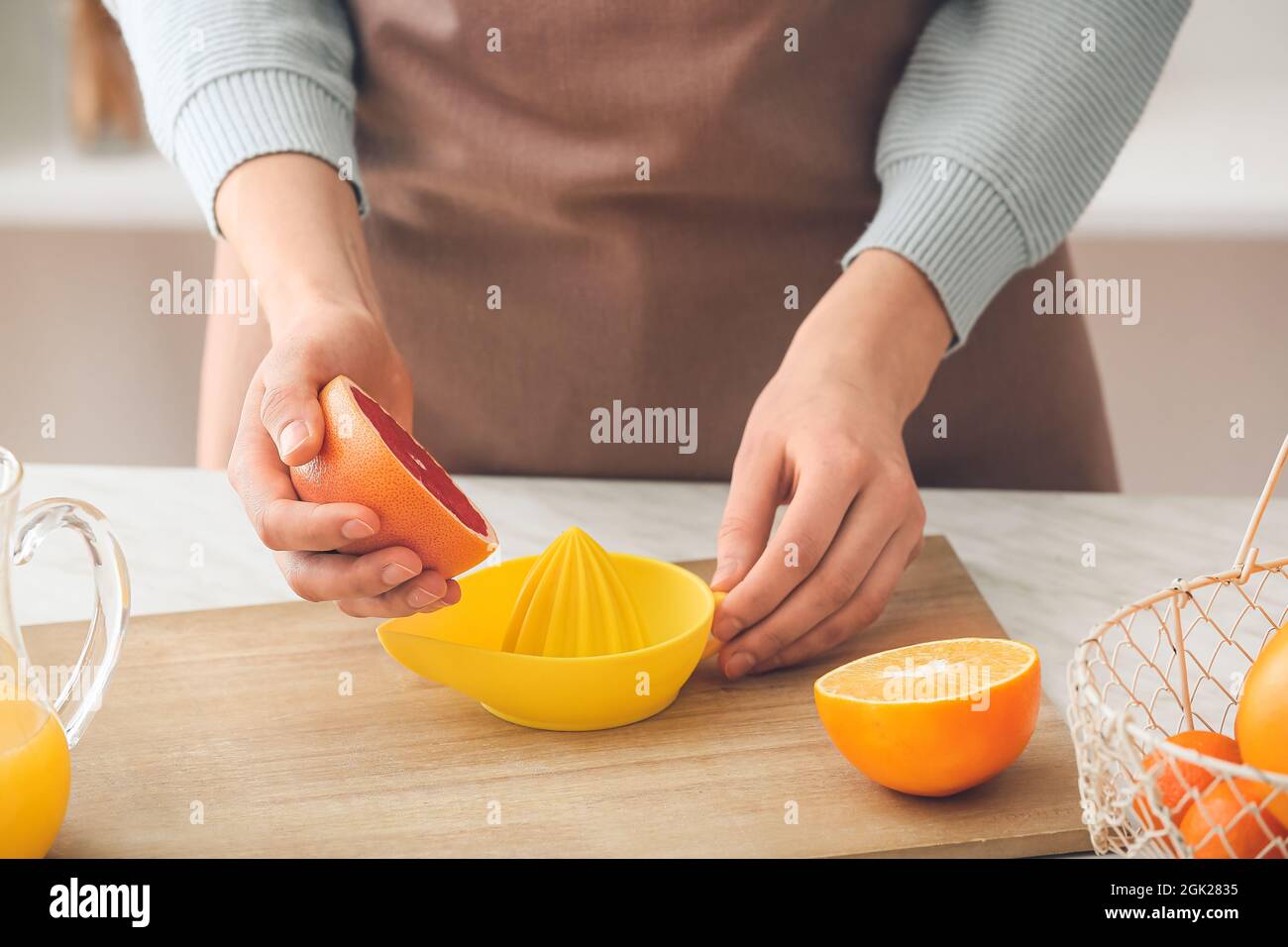 Woman squeezing grapefruit on table in kitchen Stock Photo
