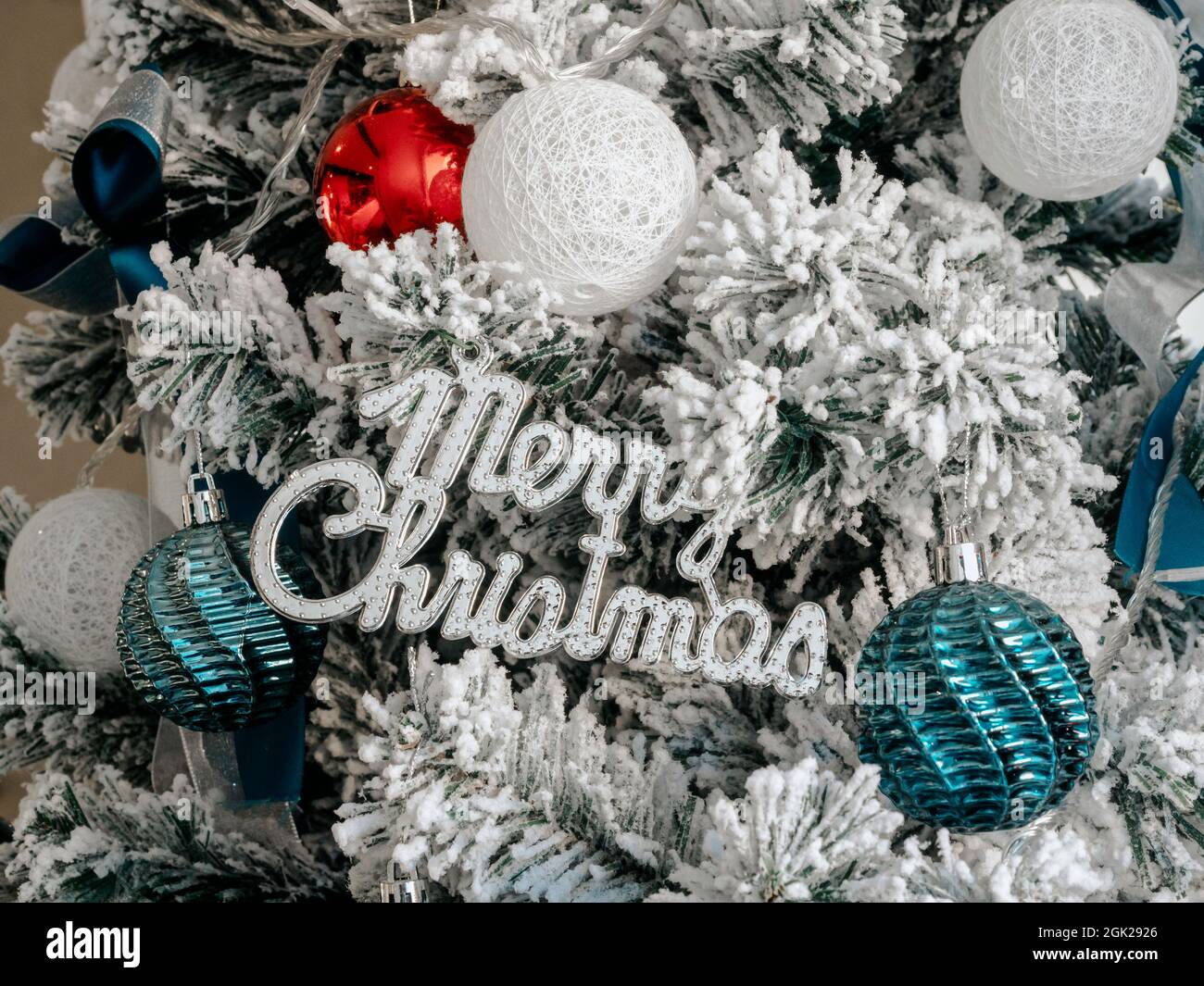 Christmas background. Merry Christmas, celebration words with balls decoration on fir tree covered by white snow, close up. Stock Photo