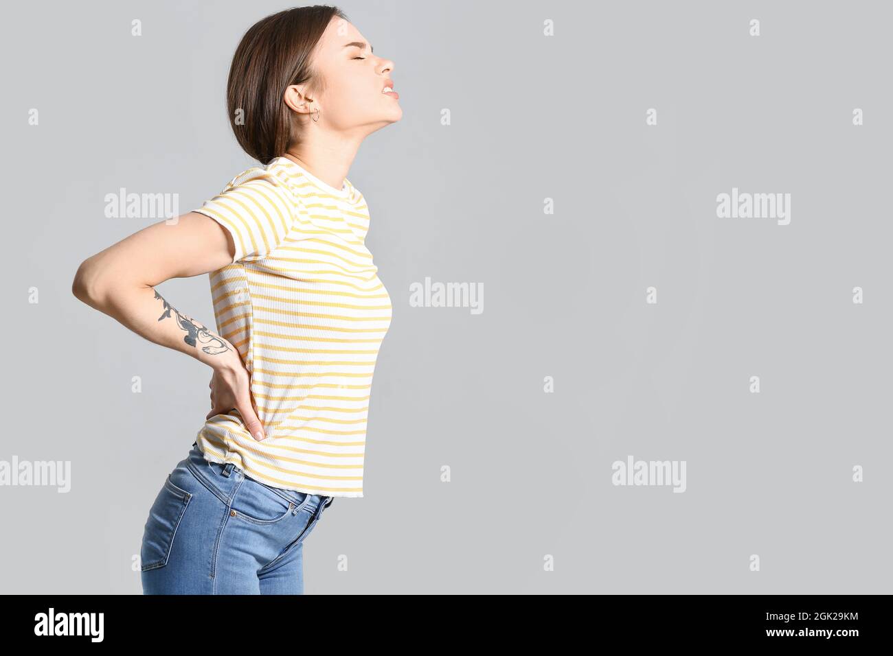 Young woman suffering from back pain on grey background Stock Photo